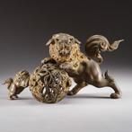 Twee tempelleeuwen die spelen met een versierde bal. -