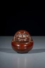 Een boxwood netsuke voorstellend een zittende Daruma-pop met