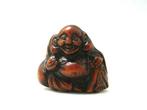 Een Netsuke met Hotei, afgebeeld terwijl hij glimlacht en de